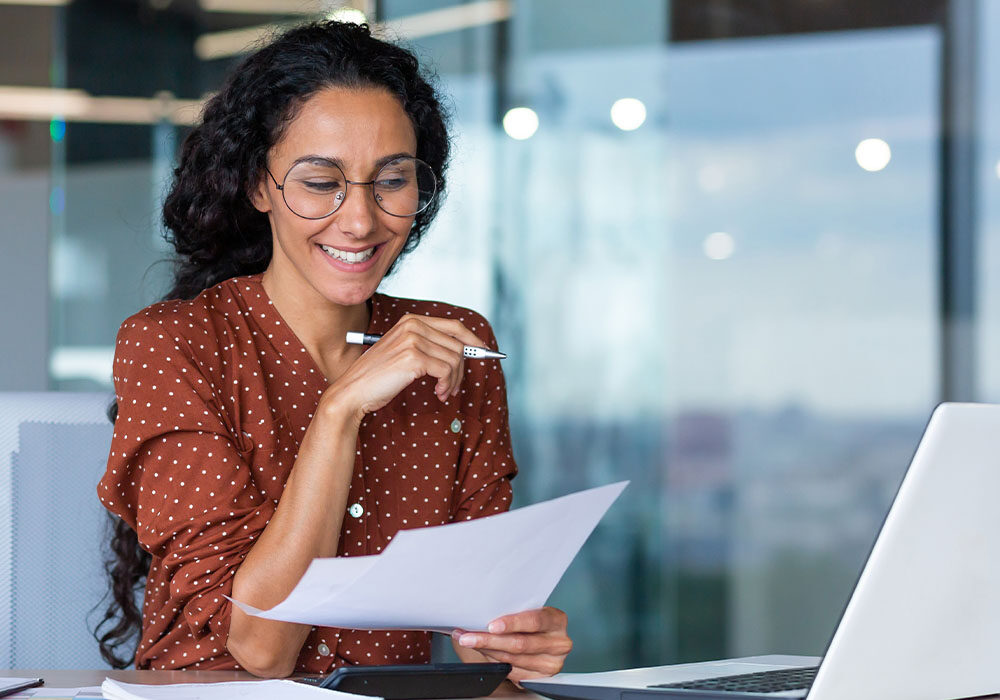 woman smiling at paperwork by laptop